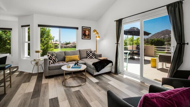 A modern living room with a sofa, coffee table, and a view of the outdoors through large sliding glass doors. - Beautifully Updated 2 Bedroom Condo with Stunning Views (La Quinta)