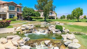 A residential area with a small waterfall, well-maintained lawns, and houses with balconies. - Beautifully Updated 2 Bedroom Condo with Stunning Views (La Quinta)