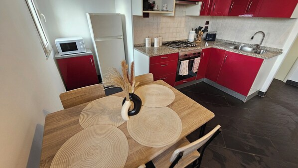 Une cuisine avec des meubles de rangement rouges, un four à micro-ondes, une cuisinière et un évier.