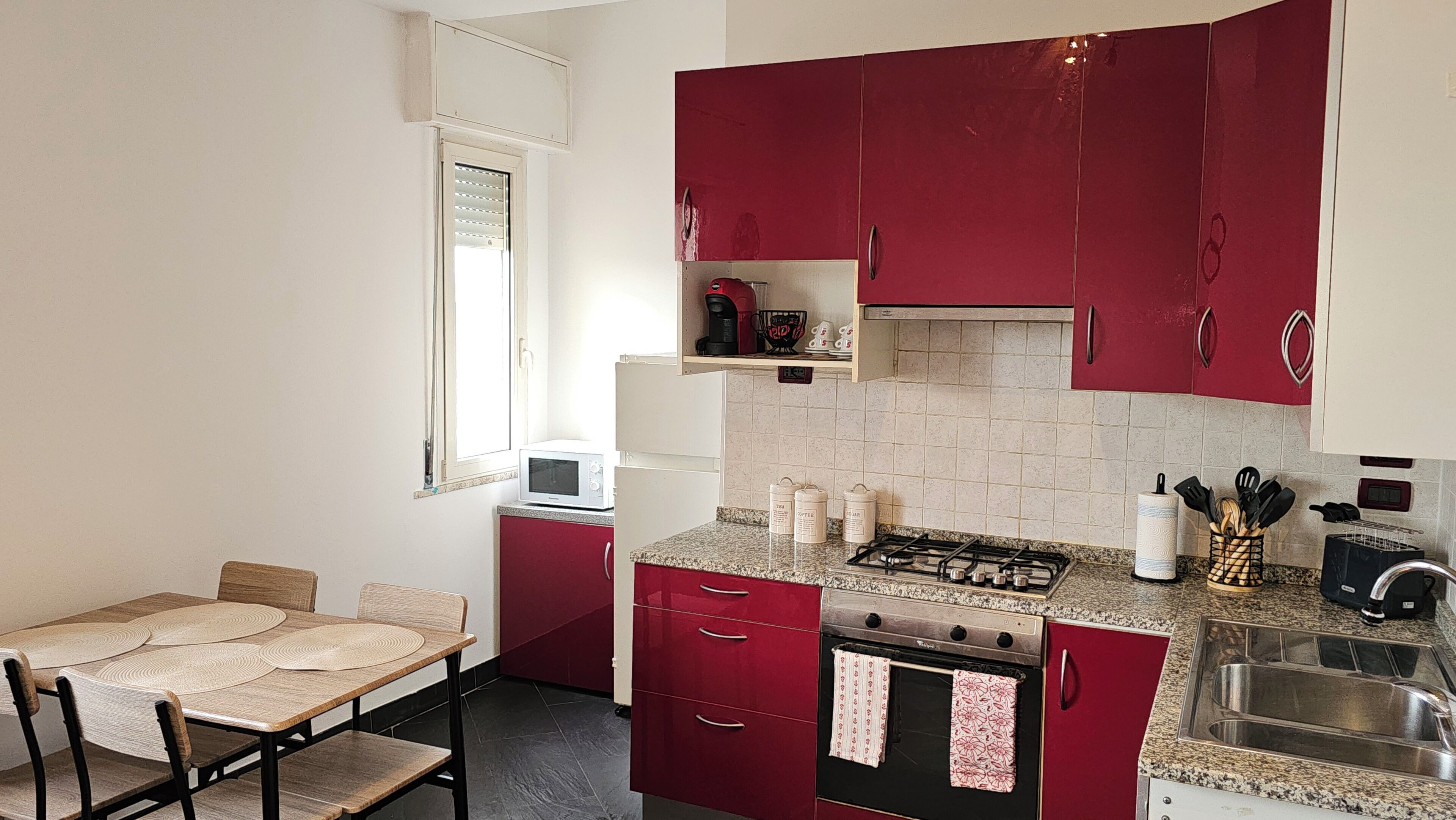 A compact kitchen with red cabinets, a gas stove, a microwave, and a small dining table with chairs.