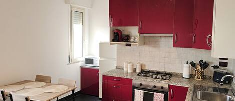 A compact kitchen with red cabinets, a gas stove, a microwave, and a small dining table with chairs.