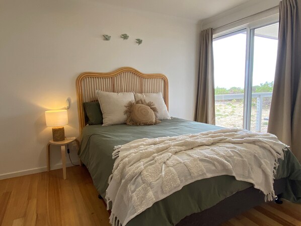 A bedroom with a bed, a bedside lamp, a window with curtains, and a view of the outdoors.