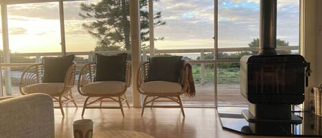 Een moderne woonkamer met rieten stoelen, een ronde houten tafel en een groot raam met uitzicht op een prachtig landschap.