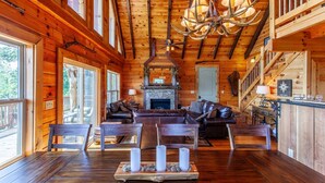 A log cabin interior with a fireplace, leather furniture, and a chandelier. - Altitude Adjustment Magnificent Custom Cabin with Breathtaking Views (Bryson City)