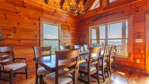 A wooden cabin with a dining area featuring a table and chairs, large windows, and a chandelier. - Altitude Adjustment Magnificent Custom Cabin with Breathtaking Views (Bryson City)