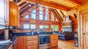 A spacious kitchen with wooden cabinets, a central island, and a stone fireplace. - Altitude Adjustment Magnificent Custom Cabin with Breathtaking Views (Bryson City)