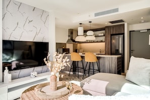 A modern living room with a flat-screen TV, a sofa, and a dining area with bar stools. - Contemporary Comfort at City Suite 905 (Cape Town)