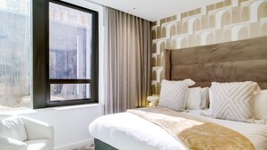 A modern bedroom with a large bed, a window with curtains, a sofa, and a patterned wall. - Contemporary Comfort at City Suite 905 (Cape Town)