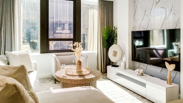 A modern living room with a large window, a flat-screen TV, a white sofa, a round coffee table, and a decorative vase. - Contemporary Comfort at City Suite 905 (Cape Town)