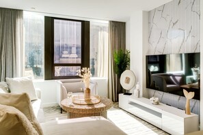 Un salon moderne doté d’une grande fenêtre, d’un téléviseur à écran plat, d’un canapé blanc, d’une table basse ronde et d’un vase décoratif.