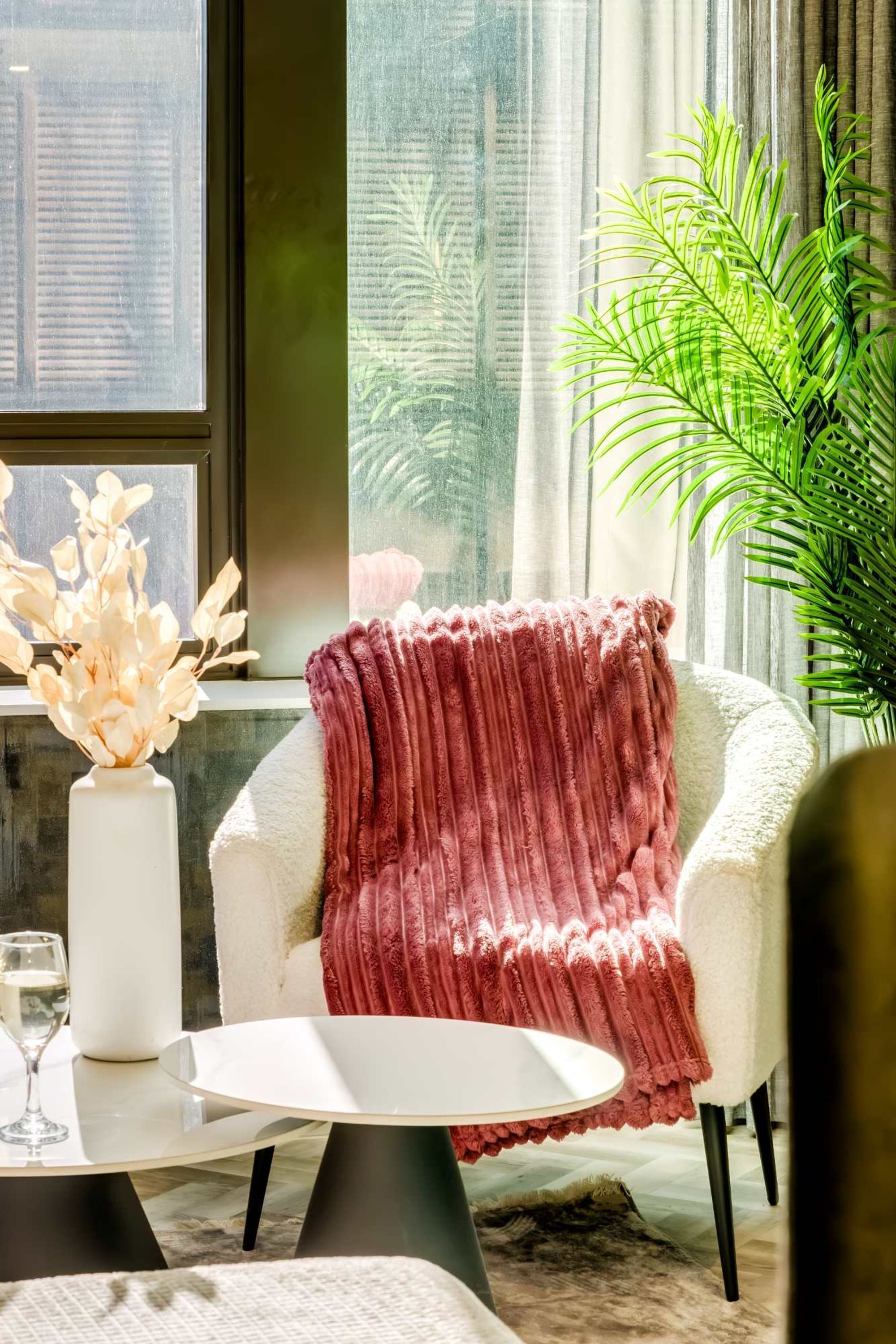 Uma sala de estar moderna com uma poltrona branca, uma mesa redonda branca e um vaso de vidro com flores secas.
