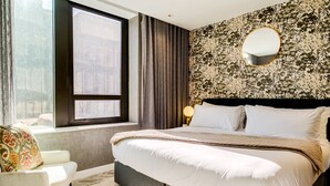 Et moderne hotelværelse med en stor seng, et vindue med gardiner, en mønstret væg og et rundt spejl.