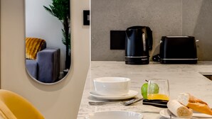 A modern kitchen with a marble countertop, a coffee maker, a toaster, and a dining area with a yellow chair and a bowl of fruit. - Upscale Urban Haven at City Suite 906 (Cape Town)