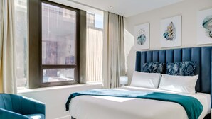 A hotel room with a large bed, a blue armchair, a window with curtains, and artwork on the wall. - Upscale Urban Haven at City Suite 906 (Cape Town)