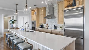 Une cuisine moderne dotée d’un grand îlot central, d’appareils électroménagers en acier inoxydable et de luminaires suspendus.