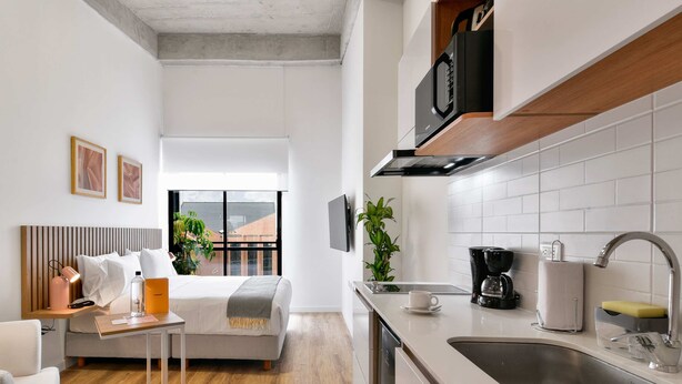 A compact hotel room with a bed, bedside table, and a kitchenette area including a sink and microwave. - w Amazing Loft w Balcony in Chapinero (Bogotá)