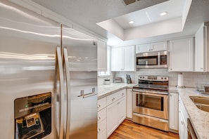 A modern kitchen with stainless steel appliances, white cabinetry, and a wooden floor.
