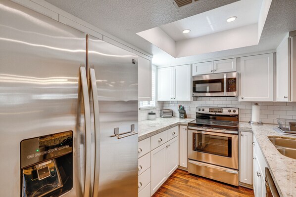 Una cocina moderna con electrodomésticos de acero inoxidable, armarios blancos y piso de madera.