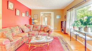 A living room with a sectional sofa, a glass coffee table, and a view of the outdoors through a window with curtains. - 1440 Getaway w/ Yard & Deck ~ 16 Mi to Rochester (Rush)