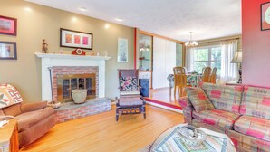 A cozy living room with a fireplace, a sofa, a chair, and a dining area with a table and chairs. - 1440 Getaway w/ Yard & Deck ~ 16 Mi to Rochester (Rush)