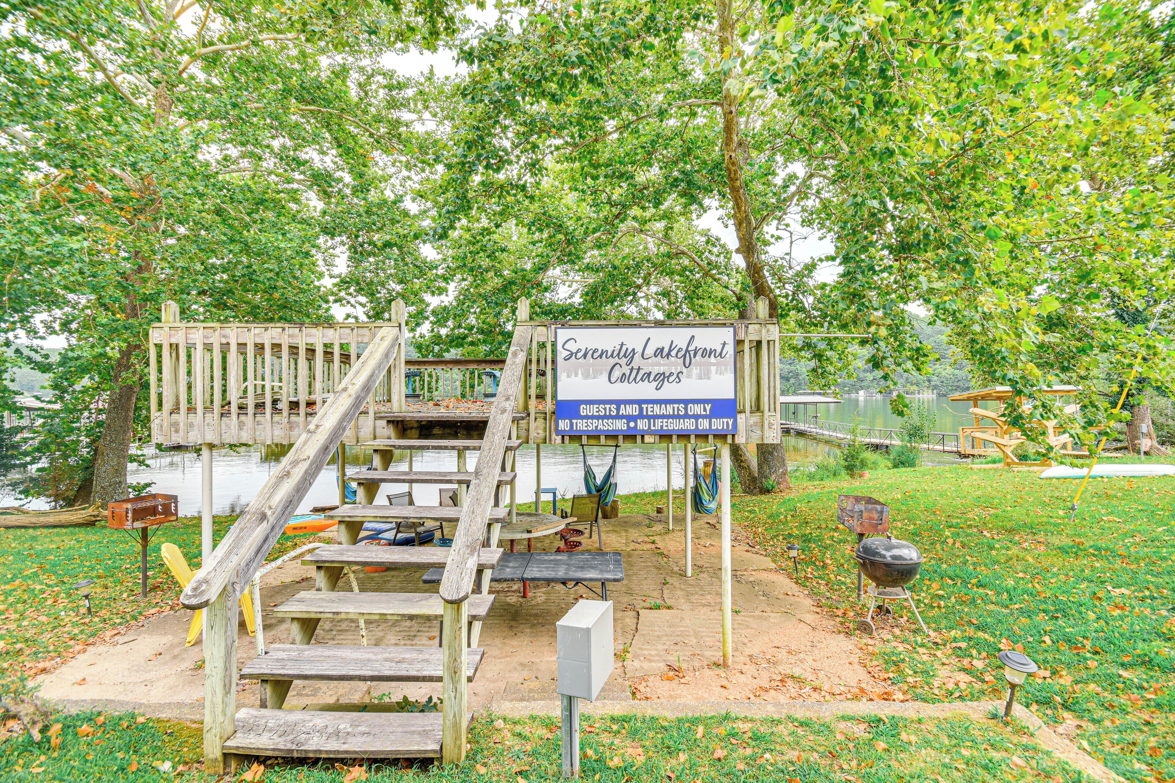 Une terrasse en bois avec une enseigne indiquant « Serenity Lakefront Cottages », une table de pique-nique et un barbecue.