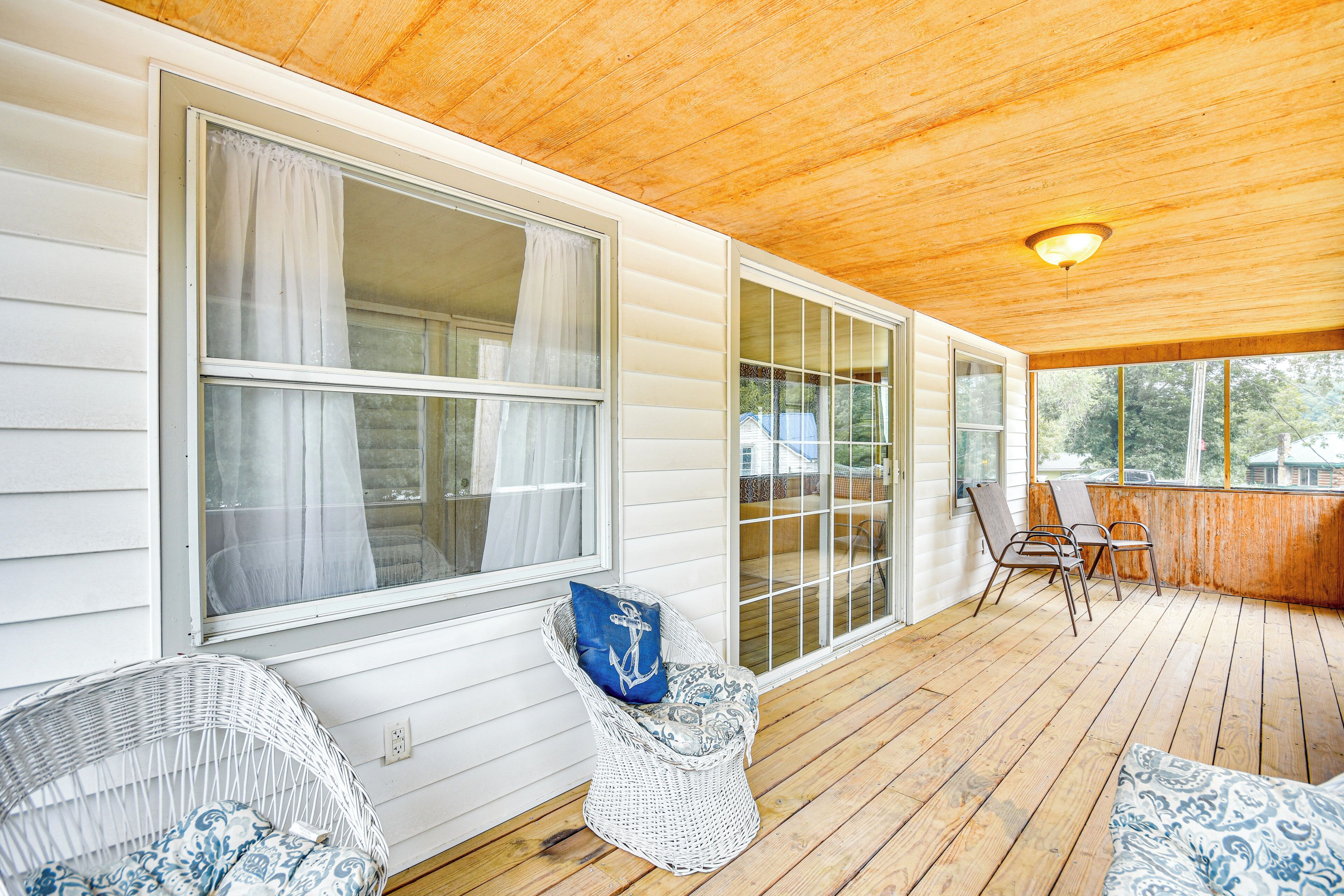 A covered porch with wicker chairs, a wooden deck, and large windows.