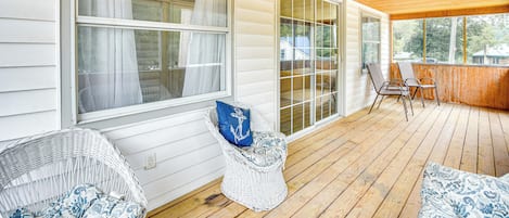 A covered porch with wicker chairs, a wooden deck, and large windows.