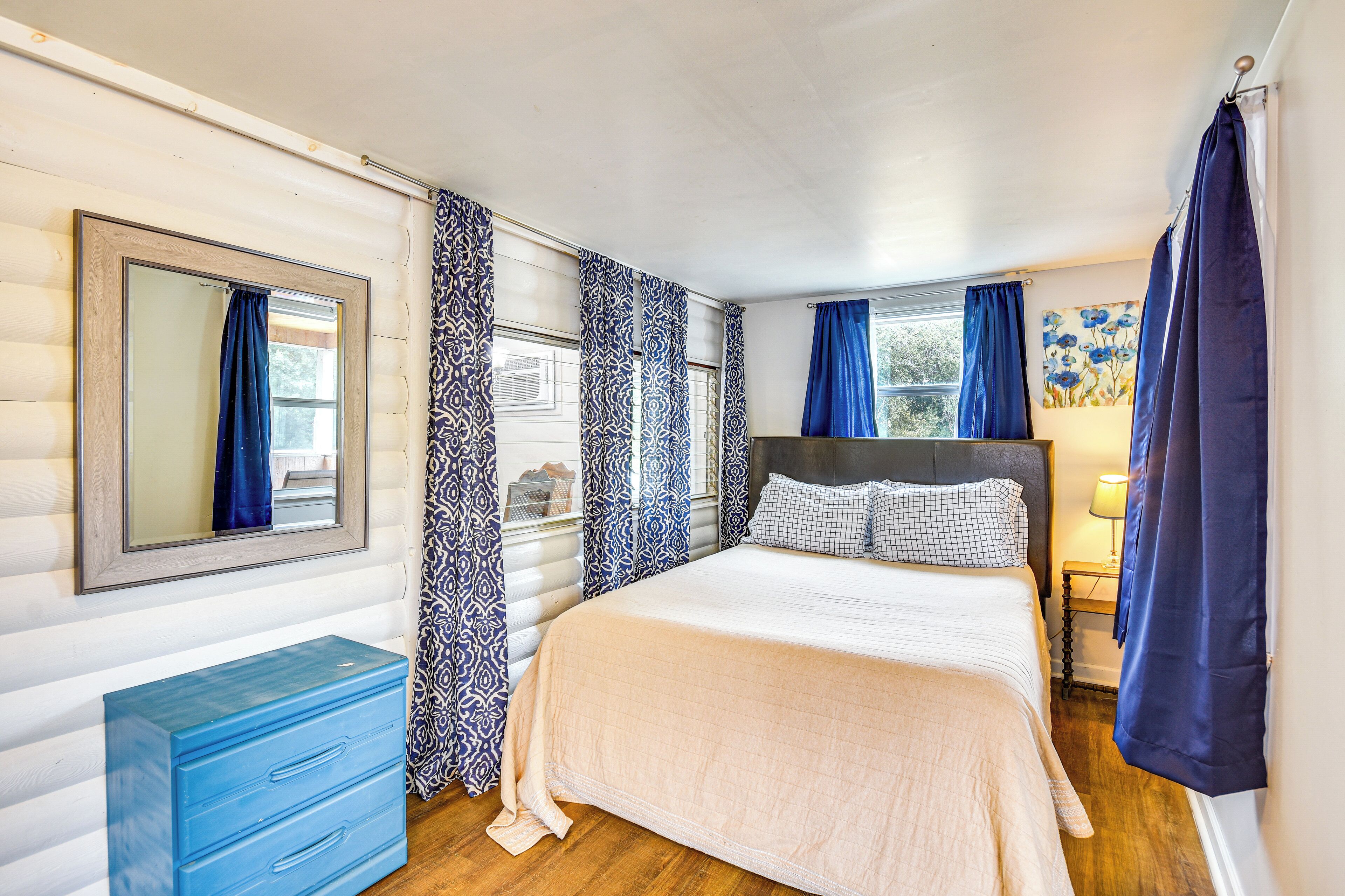 Un dormitorio con cama, cómoda, espejo y cortinas.