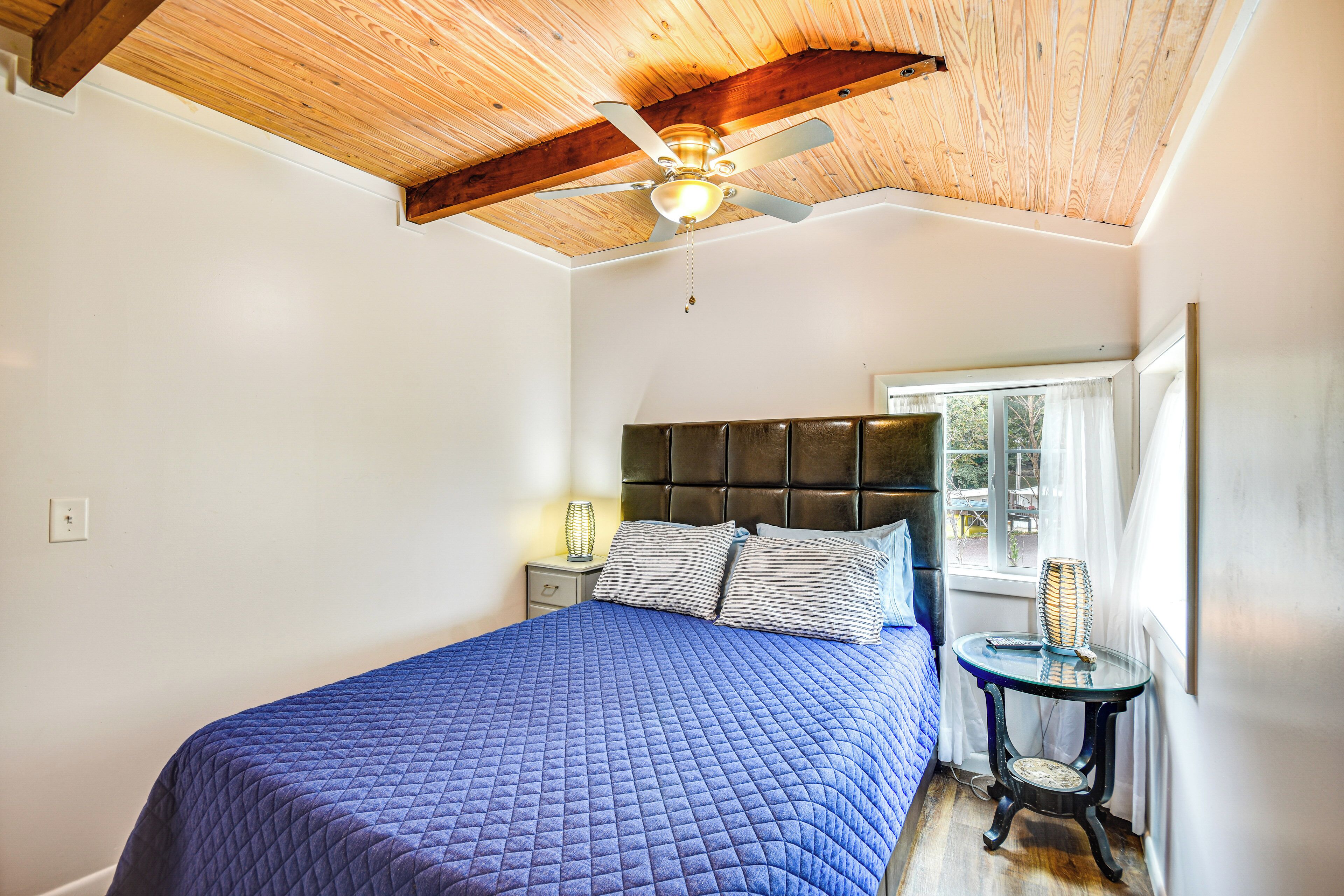 A bedroom with a bed, a nightstand, a window with curtains, and a ceiling fan.