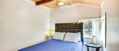 A bedroom with a bed, a nightstand, a window with curtains, and a ceiling fan.