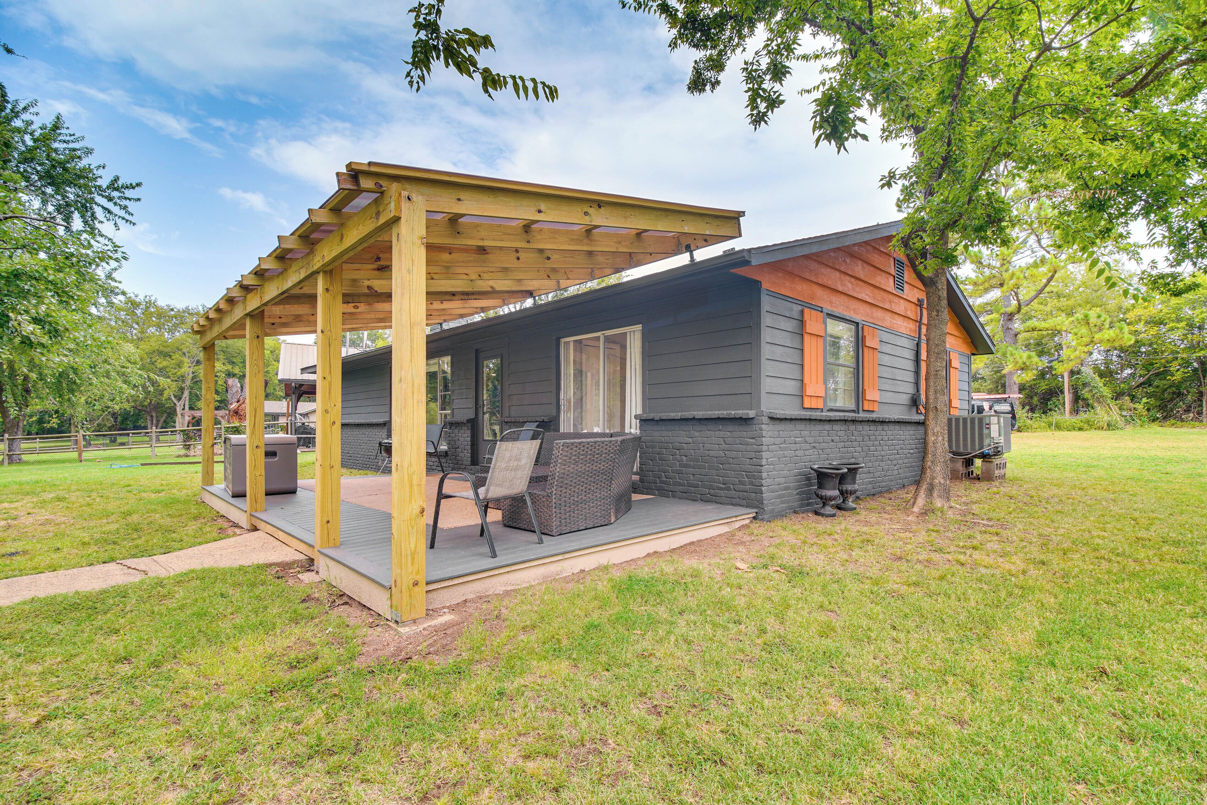 Une terrasse couverte, aménagée avec du mobilier d’extérieur, un mur en briques et une pergola en bois.