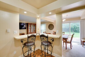 A kitchen with two bar stools, a dining table with chairs, and a large window with a view of the outdoors.