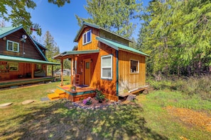A wooden cabin with a porch, a covered deck, and a small garden area with flowers. - Cabin on 5 Acres in Port Angeles w/ Fire Pit! (Port Angeles)