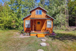 A wooden cabin with a front porch, a door, and two windows.