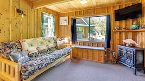Ein gemütliches Holzhaus-Interieur mit einer Couch, einer Bank, einem Fernseher und einem Fenster mit Blick auf ein Haus.