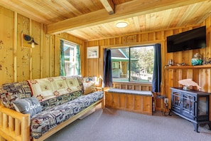 A cozy wooden cabin interior with a sofa, a bench, a television, and a window overlooking a house. - Cabin on 5 Acres in Port Angeles w/ Fire Pit! (Port Angeles)