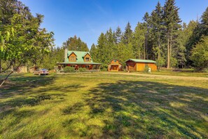 A large house with a green roof, surrounded by a grassy yard and tall trees.
