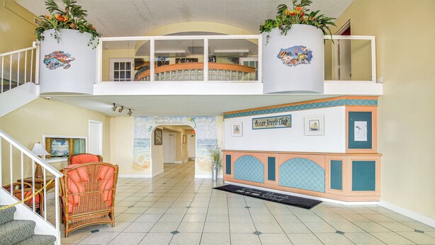 A spacious lobby with a staircase, wicker furniture, a reception desk, and a decorative wall mural. - Daytona Beach Condo w/ Balcony: 5 Mi to Speedway! (Daytona Beach)
