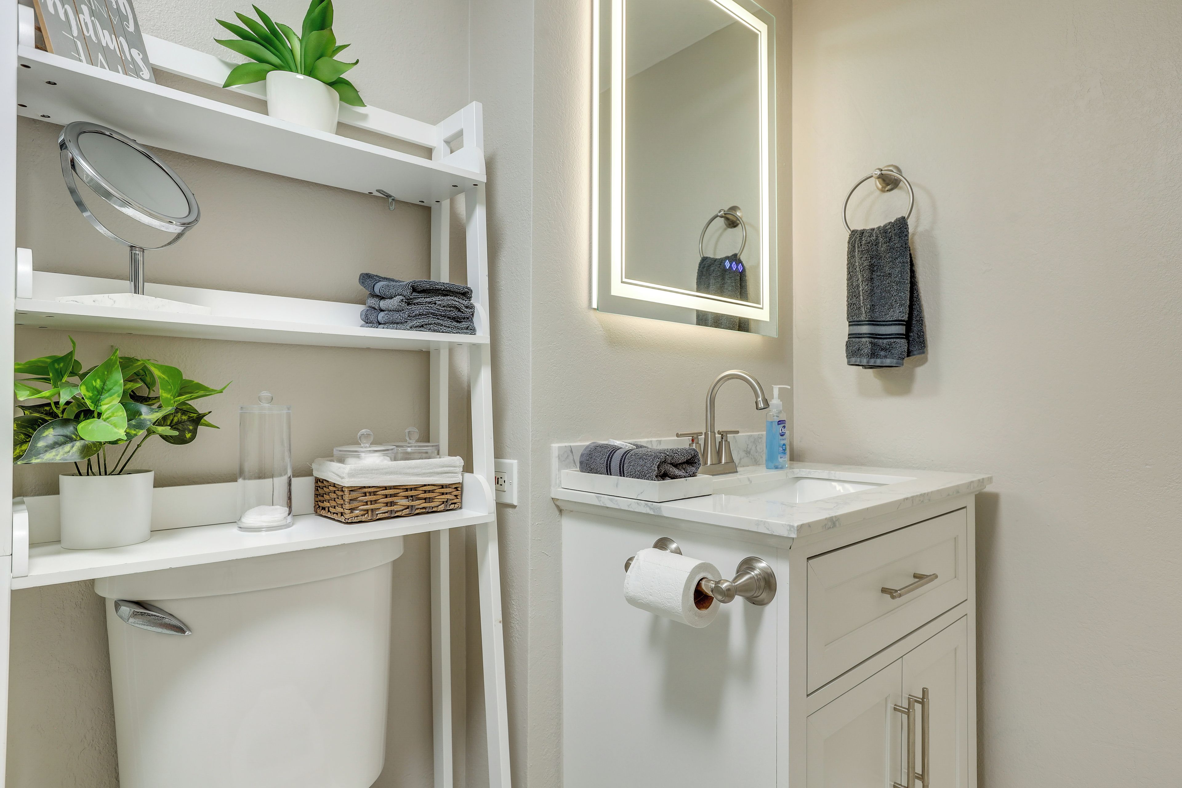 A bathroom with a white vanity, a mirror, a towel rack, and a shelf with toiletries.