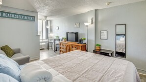 A bedroom with a large bed, a desk, a television, and a sign on the wall. - Daytona Beach Condo w/ Balcony: 5 Mi to Speedway! (Daytona Beach)