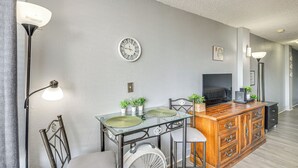 A modern living room with a glass-top dining table, a wooden cabinet, a TV, and a ceiling fan. - Daytona Beach Condo w/ Balcony: 5 Mi to Speedway! (Daytona Beach)