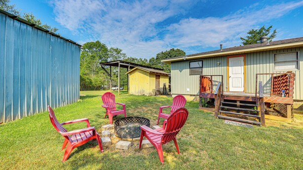 Ein Garten mit Feuerstelle, roten Adirondack-Stühlen und einer Holzterrasse.
