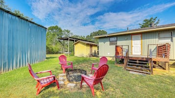 Quintal com lareira, cadeiras Adirondack vermelhas e um deck de madeira.