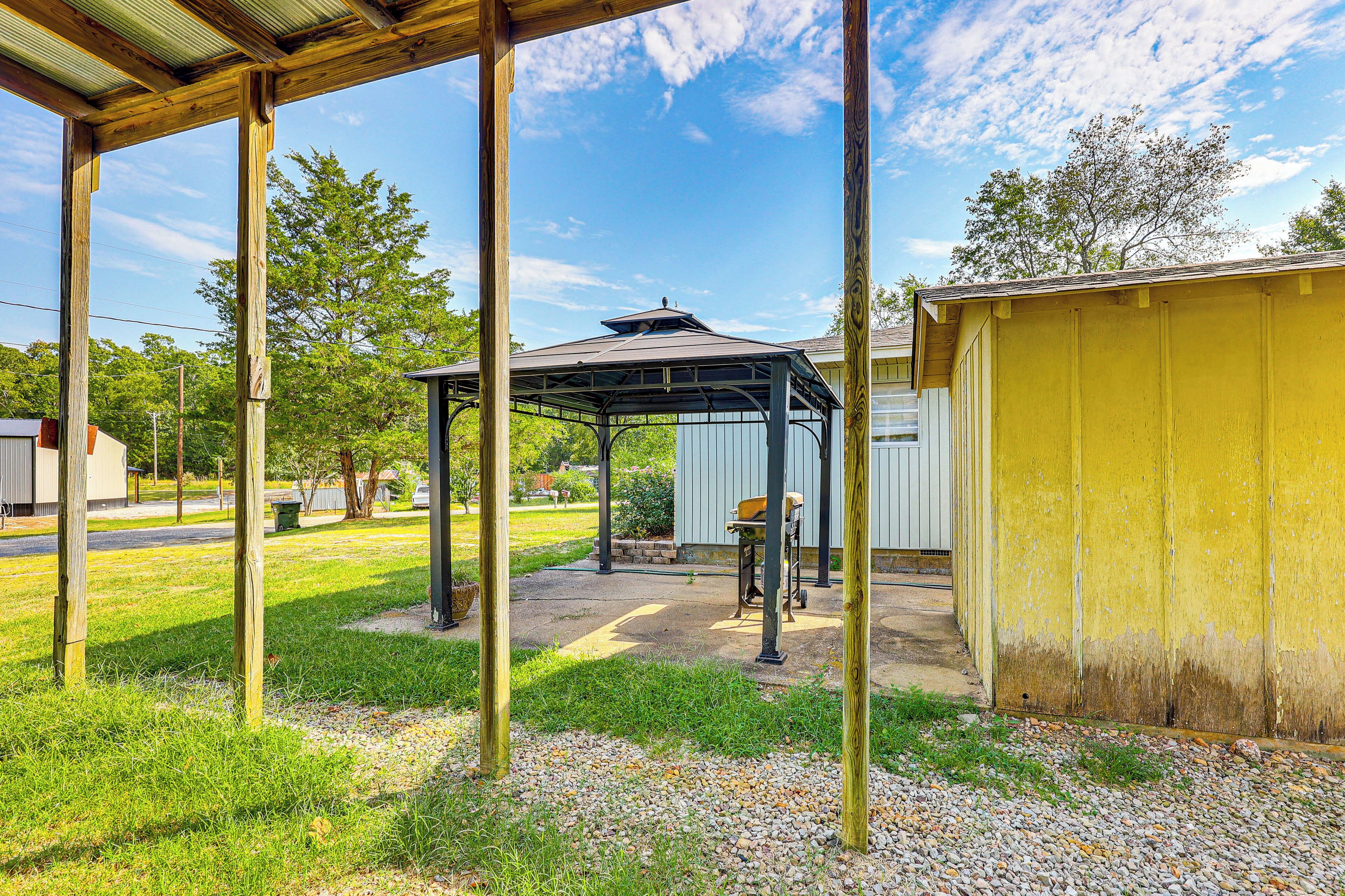 Un espacio al aire libre cubierto con una pérgola, un edificio amarillo y un camino de grava.