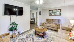 Ein Wohnzimmer mit Deckenventilator, Flachbildfernseher, braunem Sofa, Couchtisch und einem gemusterten Teppich.