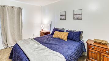 Quarto com cama, mesa de cabeceira, cômoda e duas imagens penduradas na parede.
