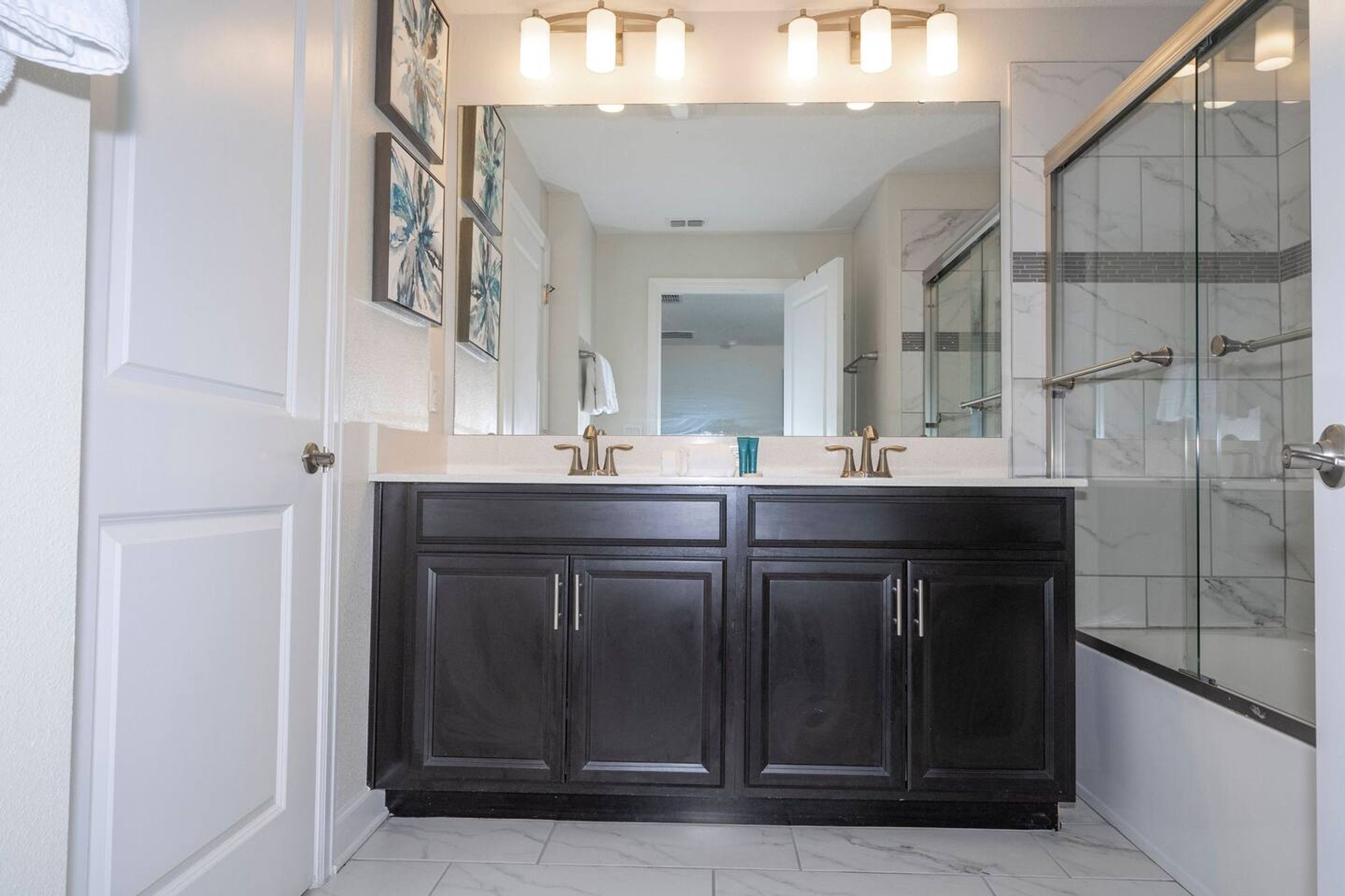 A bathroom with dark wood cabinets, a white countertop, a large mirror, and a glass shower enclosure.