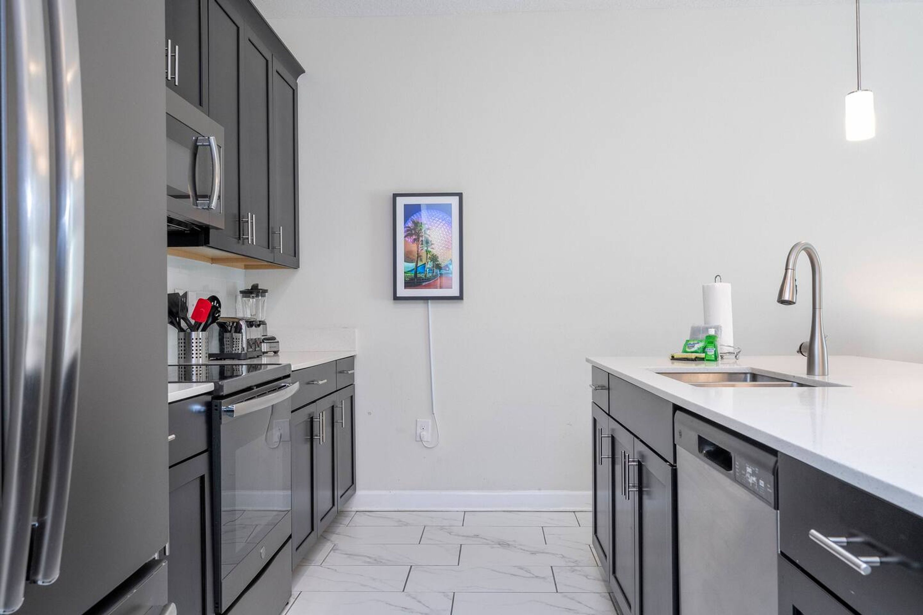 A modern kitchen with stainless steel appliances, a white countertop, and a single hanging picture.