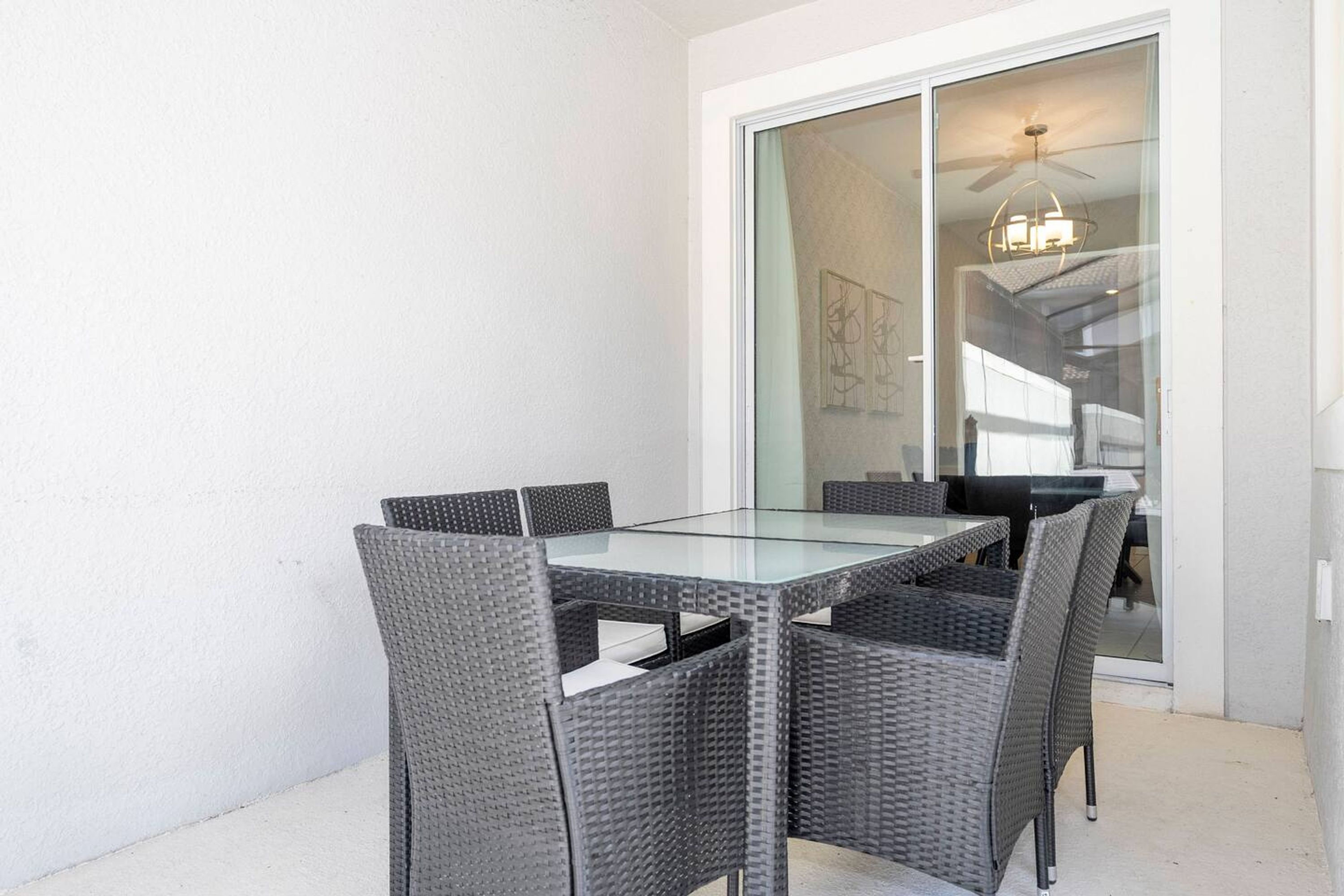 A glass-top table with four wicker chairs in a room with a sliding glass door leading to a balcony.