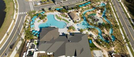 An aerial view of a resort with a large swimming pool, multiple lounge areas, and a road surrounding the property.